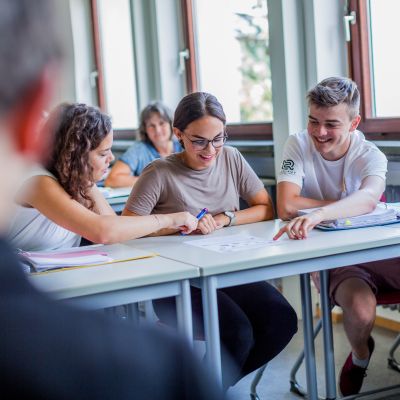 Zwei Schüler*innen die einer Schülerin etwas zeigen