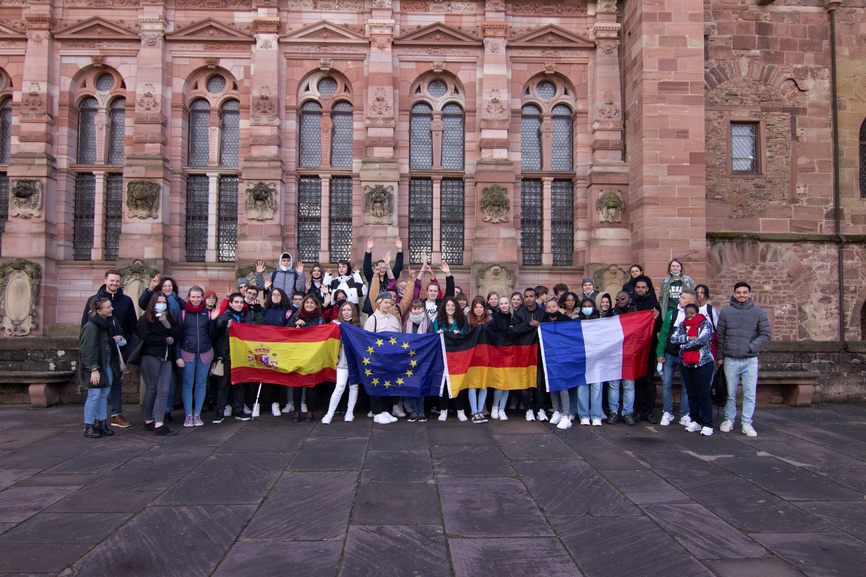 Auf dem Bild sieht man mehrere Personen die vor einem alten Gebäude stehen und vier Flaggen halten.